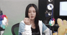 a girl is sitting in front of a microphone and making a heart shape with her finger