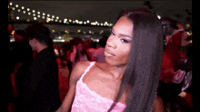 a woman in a pink lace dress stands in a crowded room