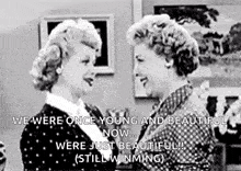 two women are standing next to each other in a living room and talking to each other .