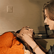 a woman in an orange sweater is touching another woman 's hair