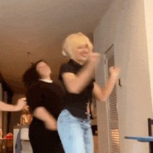two women are dancing together in a room and one of them is wearing a blonde wig .