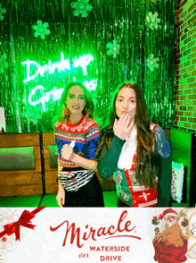 two women standing in front of a miracle on waterside drive sign