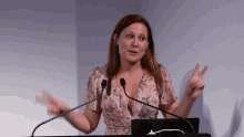 a woman in a floral dress is giving a speech at a podium