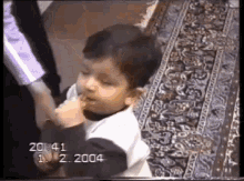 a young boy is sitting on a rug and eating a piece of food
