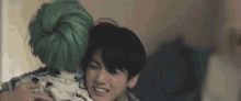 a man with green hair is hugging another man in a bedroom .