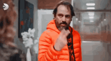 a man in an orange jacket is giving the middle finger to a woman .