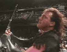 a man with a mullet and a pink jacket is holding a trophy in front of a crowd .