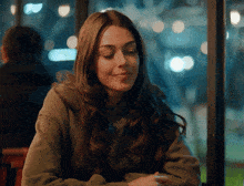 a woman in a green sweatshirt sits at a table at night