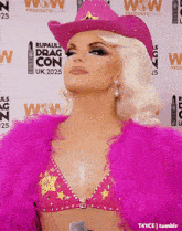 a woman wearing a pink cowboy hat is standing in front of a wall that says wow on it