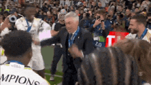 a man in a suit is surrounded by soccer players wearing champions uniforms