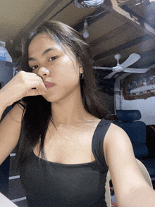 a woman in a black tank top is taking a selfie in front of a ceiling fan