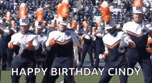 a marching band is dancing on a field with the words happy birthday cindy in the background .