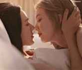 two women kissing on a bed with a watermark that says unicorngifs