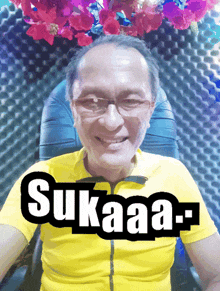 a man wearing glasses and a yellow shirt with the word sukaaa above him