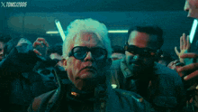 a man in glasses stands in front of a crowd with the year 2005 on the bottom left