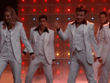 a group of men and women in white suits are dancing