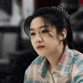 a close up of a woman 's face wearing a plaid shirt and ponytail