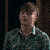 a young man in a plaid shirt has a mullet on his head
