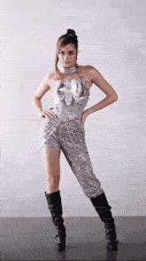 a woman in a silver dress and black boots is standing in front of a wall .