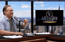 a man speaking into a microphone in front of an anthony cumia television