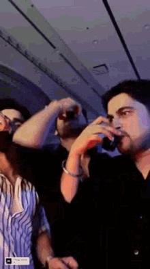 a man is drinking from a glass while standing next to another man in a dark room .