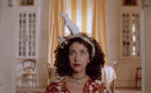 a woman with curly hair holds a white mouse on her head