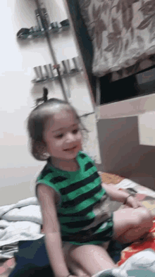 a little girl is sitting on a bed wearing a green and black striped shirt