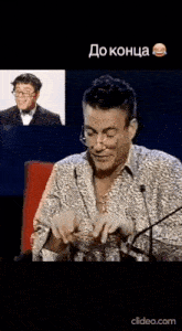a man with glasses is sitting in front of a microphone and making a funny face .