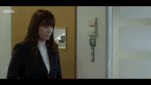 a woman in a suit stands in front of a door with bbc written on it