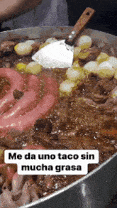 a large pot of food with a spatula and the words me da uno taco sin mucha grasa