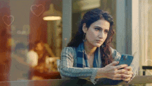 a woman looking out a window at her phone with hearts behind her
