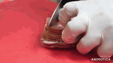 a person wearing gloves is cutting bacon on a red cutting board