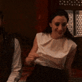 a woman wearing a white top and black skirt smiles while sitting next to a man
