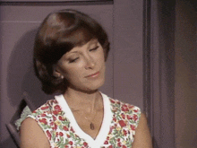 a woman wearing a floral shirt and a necklace looks down at something