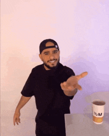 a man with a beard is standing in front of a cup of coffee and reaching out his hand .