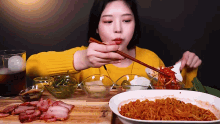 a woman in a yellow sweater is eating noodles and meat with chopsticks