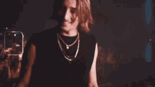 a man with long hair and a necklace is smoking a cigarette in a dark room .