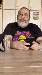 a man with a beard is sitting at a table holding a cell phone .