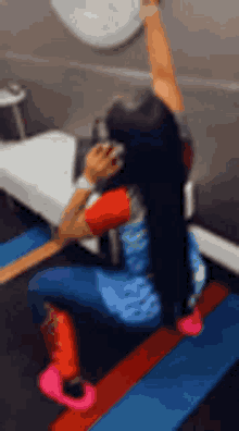 a woman is kneeling down on a mat in a gym holding a barbell over her head .