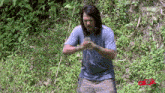 a man with long hair and headphones is standing in the grass holding a fishing rod .