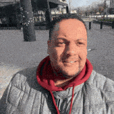 a man wearing a grey jacket and a red hoodie is smiling