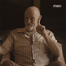 an older man is sitting in a chair with his finger in his ear and a max logo in the background