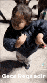 a baby in a blue jacket is standing on a sidewalk with a person holding him .