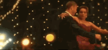 a man is holding a woman in his arms while they are dancing in front of a string of lights .