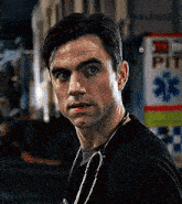 a man wearing a black shirt and a stethoscope around his neck is standing in front of an ambulance .