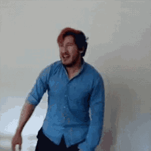 a man with red hair and a blue shirt is standing in front of a wall .
