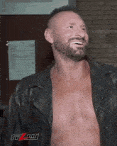 a shirtless man in a leather jacket is smiling in front of a wall with a sign that says mzn