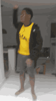 a man wearing a yellow shirt and a black jacket is standing in a room .