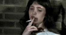 a woman is smoking a cigarette with her eyes closed in front of a brick wall .