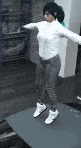 a woman in a white shirt and gray pants jumps in the air